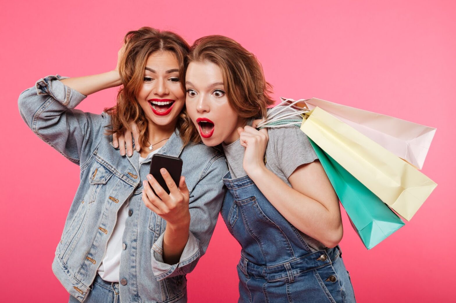 Shocked two women holding shopping bags and using mobile phone