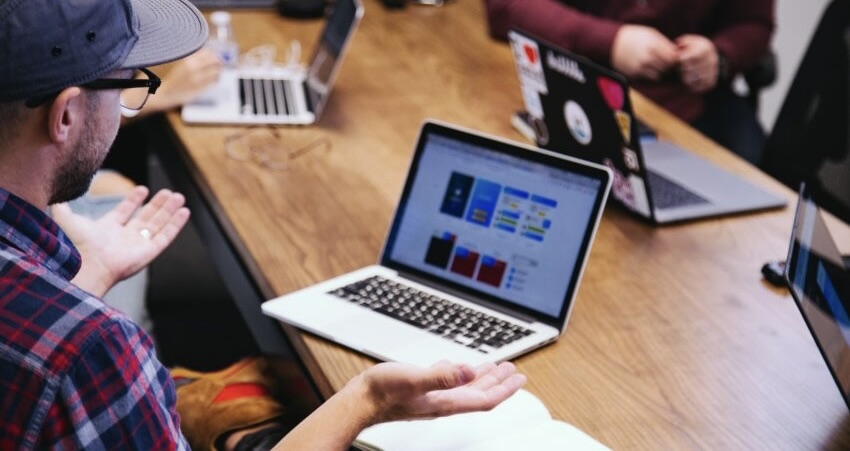 A man sits at a laptop and spreads his hands